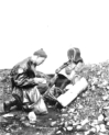 Inspecting and recording the remains of a fallen Japanese soldier on Attu. There appears to be a fencing mask and attire in the rubble.  [George Villasenor]