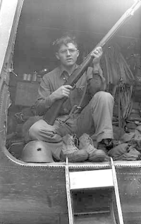 Umnak, 1943, at the door of a C-47 which evacuated some Attu casualties. All suffering frost bite except one who had a shrapnel wound under his chin. The equipment I am holding came from a deceased Jap. Note the hold in the helmet.  [Don Blumenthal]