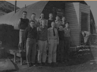 A group of 11 men standing by a Quonset (Pacific?) Hut. [ Robert Arnts]